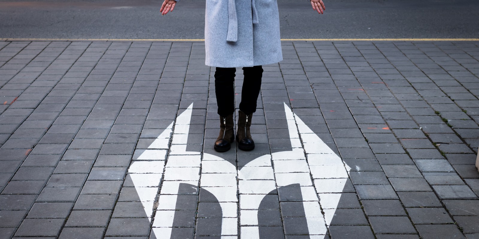 Kuvassa nainen seisoo kadulla. Hänen jalkojen juureen on maalattu kaksi eri suuntaan vievää nuolta. Kumpaan suuntaan kannattaa kääntyä? Kannattaako podcastien tekeminen vai ei? – Suomen Podcastmedia